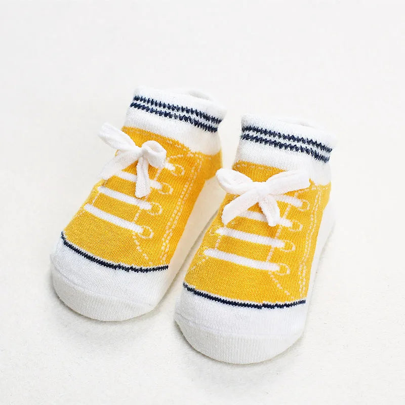 Pair of yellow baby socks styled like sneakers with white bows and striped cuffs, featuring anti-slip soles for crawling and first steps.